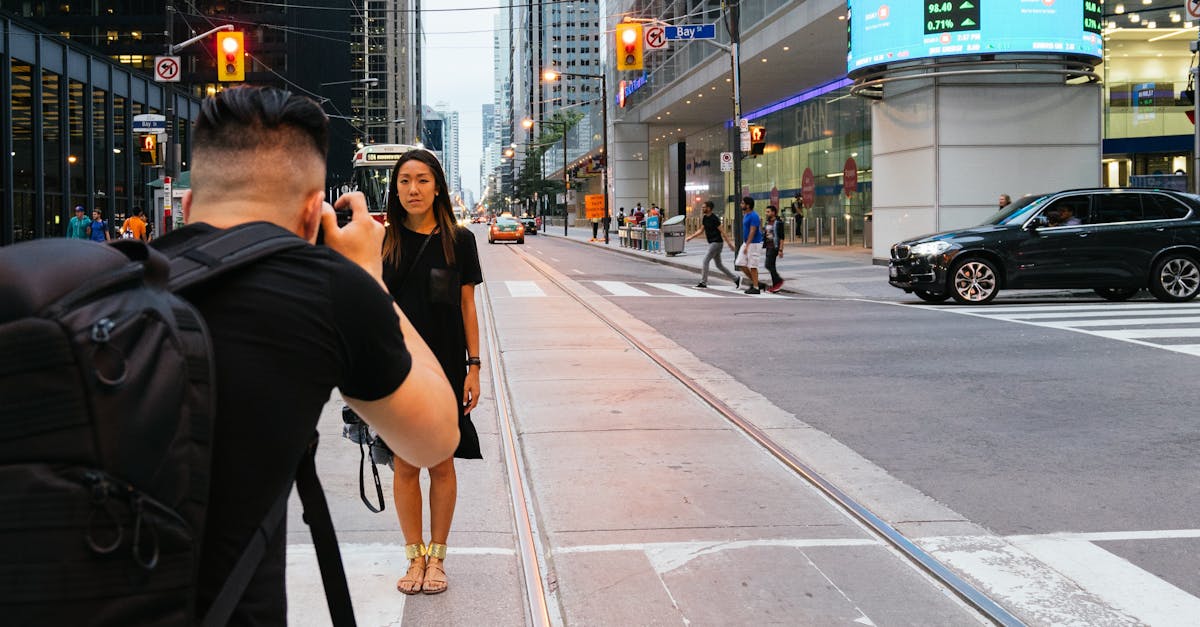 Man Taking Photo of Woman Standing Beside Highway Near Building
