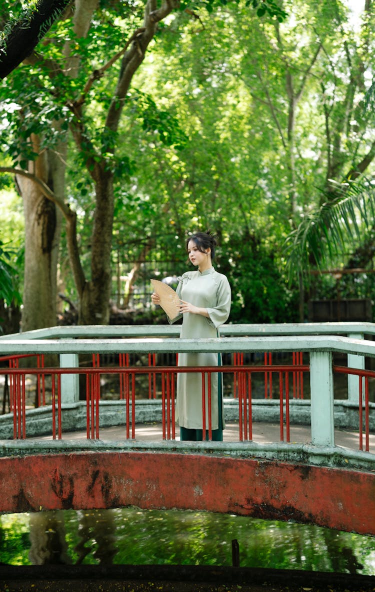 Young Woman In Traditional Dress Standing On Bridge In Summer Park