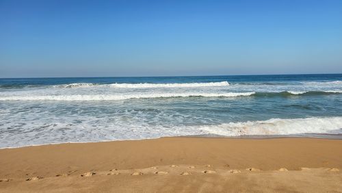 Free Golden sand beach with gentle waves and clear blue skies, ideal for summer escapes. Stock Photo