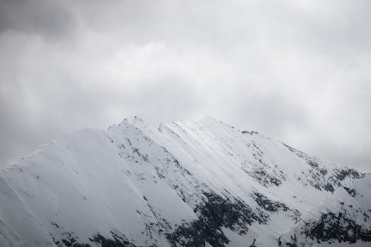 Dramatic snow-covered mountain peaks in Tirol, Austria, under a cloudy winter sky.