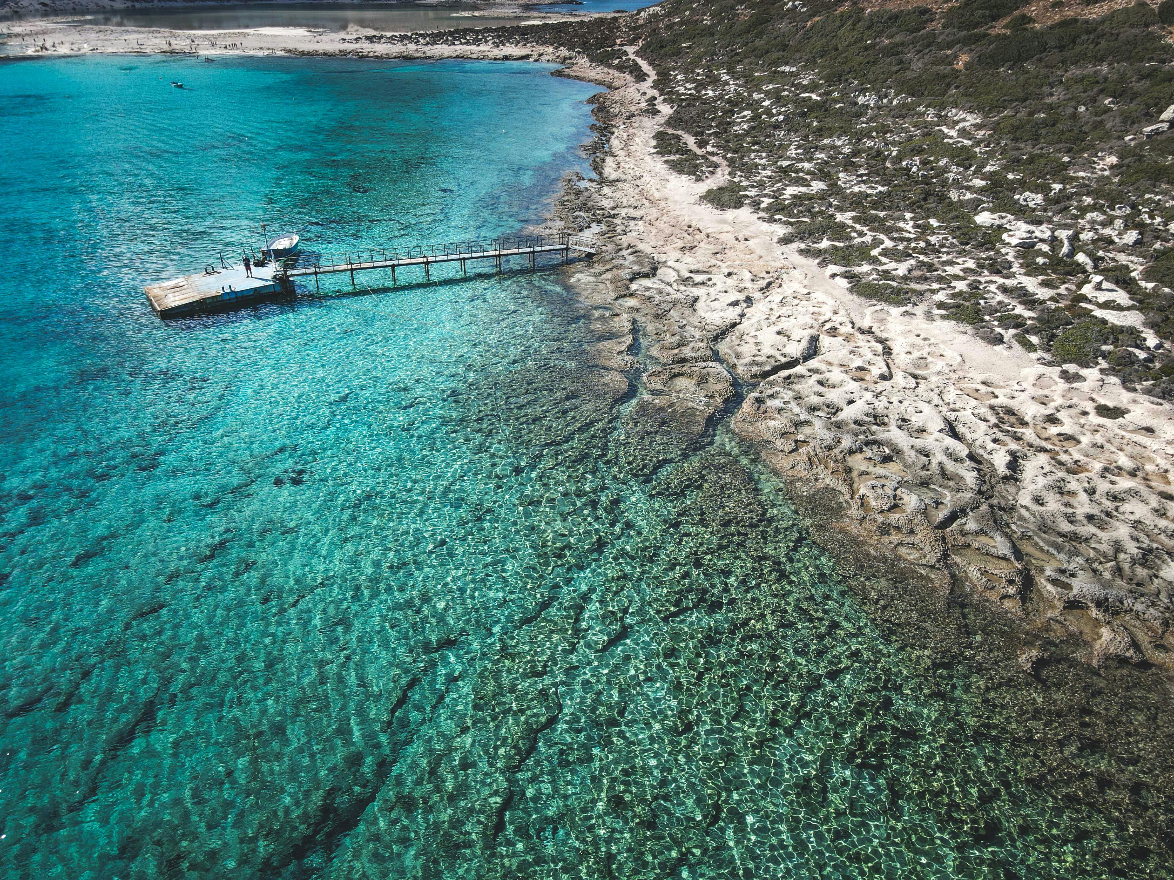 Stunning aerial view of a clear turquoise sea and sandy beach with a wooden pier.
