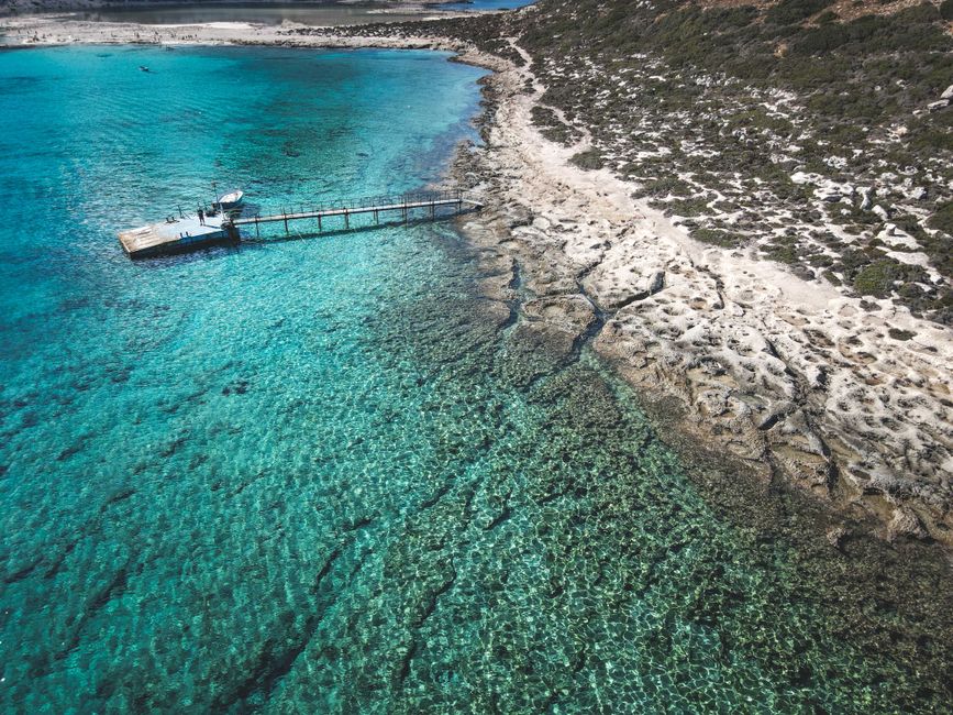 Stunning aerial view of a clear turquoise sea and sandy beach with a wooden pier.