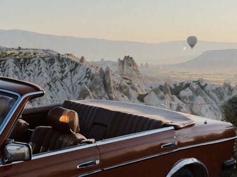 Vintage car with a hot air balloon in Cappadocia's stunning rock formations at sunset.