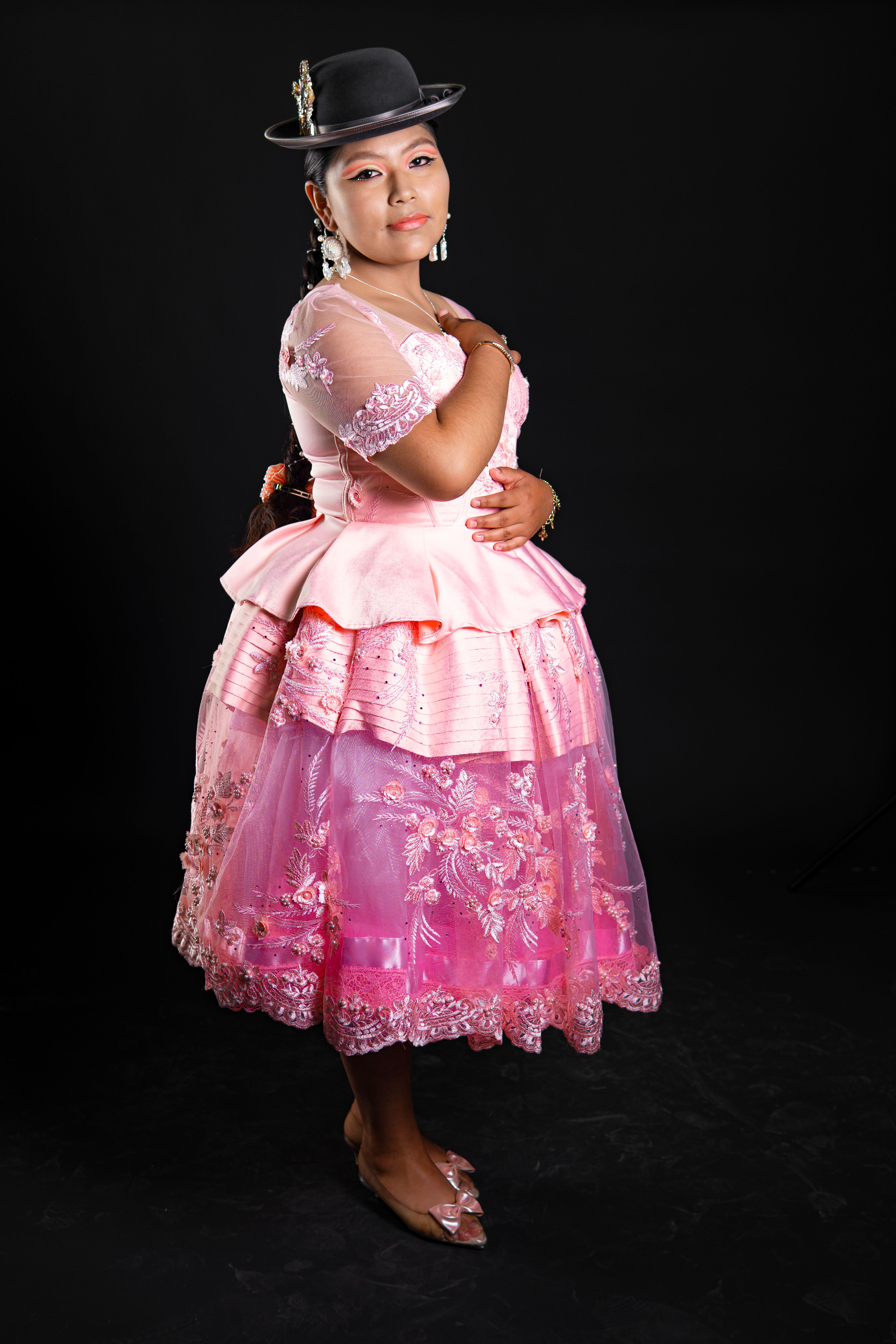 Portrait of a woman in traditional pink clothing with black hat against a black background.