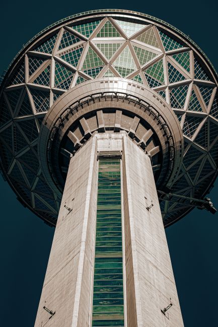 A dramatic upward view of the iconic Milad Tower against a clear sky in Tehran, Iran.