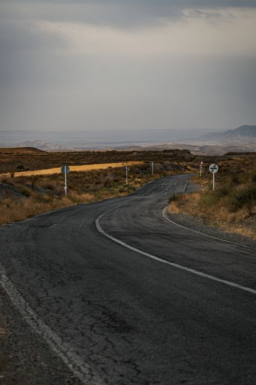 Free A deserted winding road through arid landscape on an overcast day, ideal for travel themes. Stock Photo
