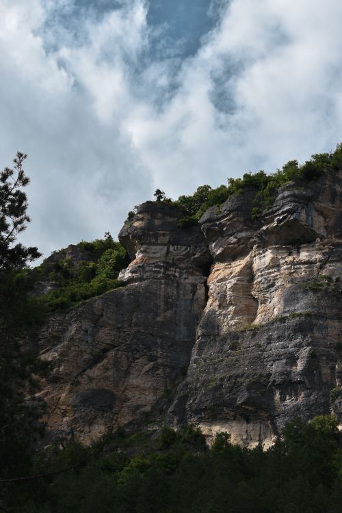 Free Majestic view of a rocky cliff with lush greenery beneath a blue sky and white clouds. Stock Photo