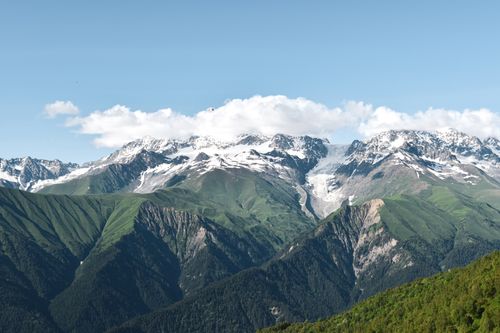 Free Breathtaking panorama of a snowcapped mountain range with a green valley in summer. Stock Photo