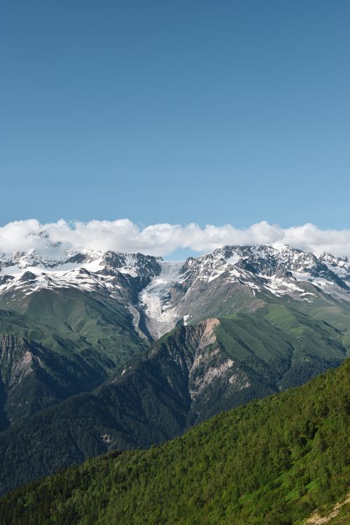 Free Breathtaking view of snow-capped mountain peaks and lush green valleys under a clear blue sky. Stock Photo