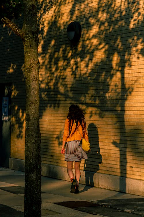 Woman in Skirt Walking near Building Wall