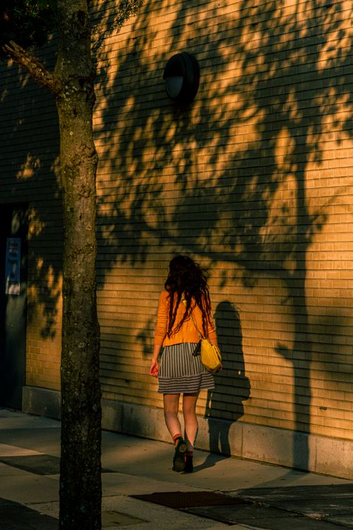 Free Silhouette of a woman walking by a sunlit wall creating interesting shadows on the sidewalk. Stock Photo