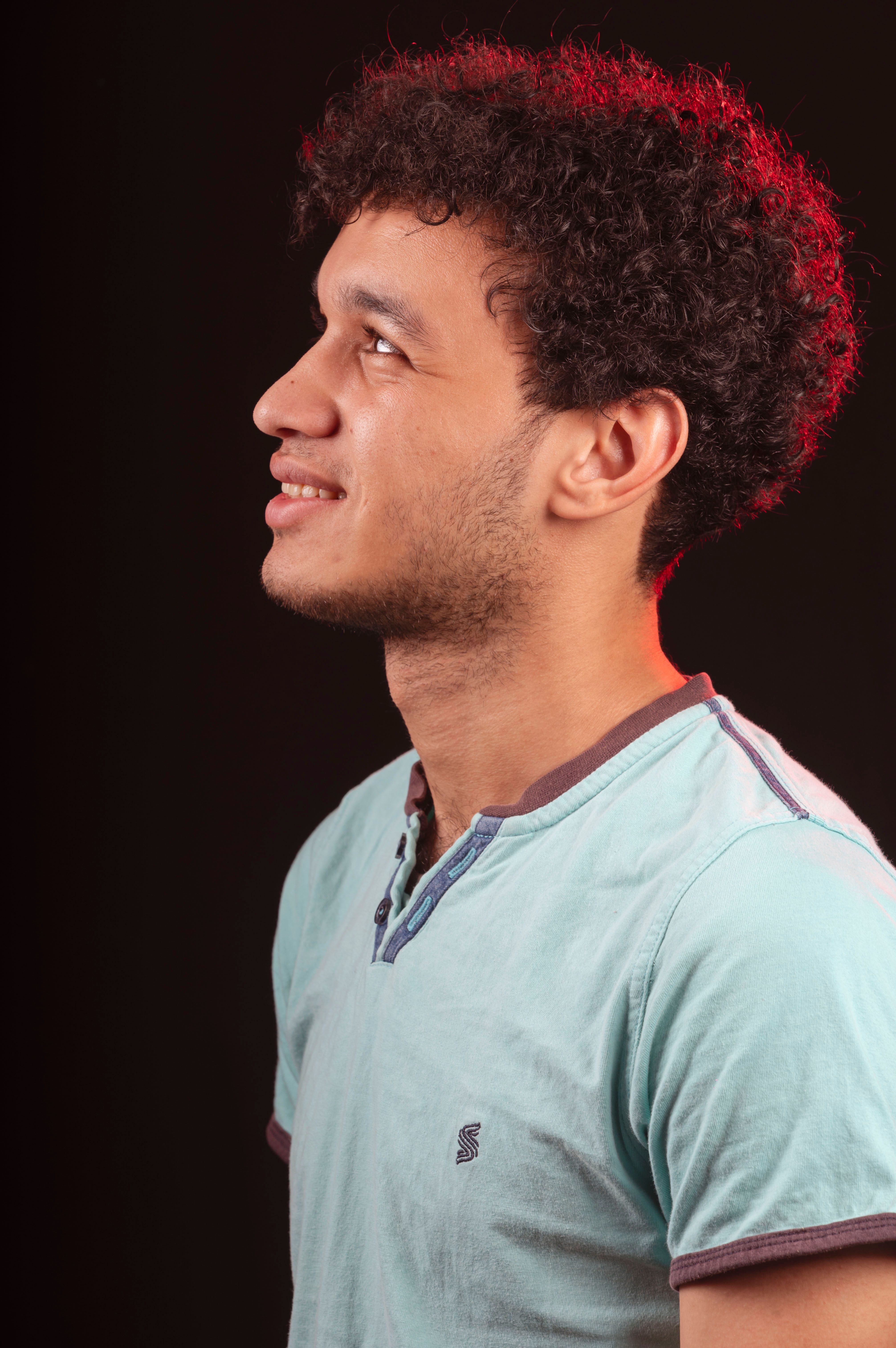Studio portrait of a smiling man with curly hair looking upwards, featuring a black background.