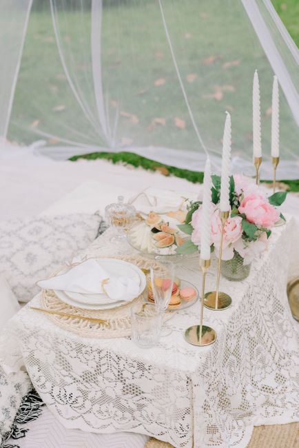 Lace-covered picnic table with candles, flower arrangement, and outdoor setting.