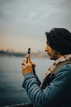 An adult man photographs the Bosphorus in Istanbul, Türkiye with a smartphone.