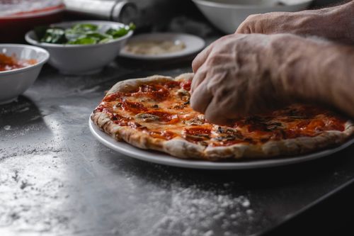 Free Close-up of man's hands preparing a freshly cooked pizza with toppings in the kitchen. Stock Photo