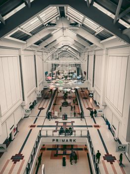 High-angle view of a spacious modern shopping mall interior with unique geometric ceiling art and several shoppers.