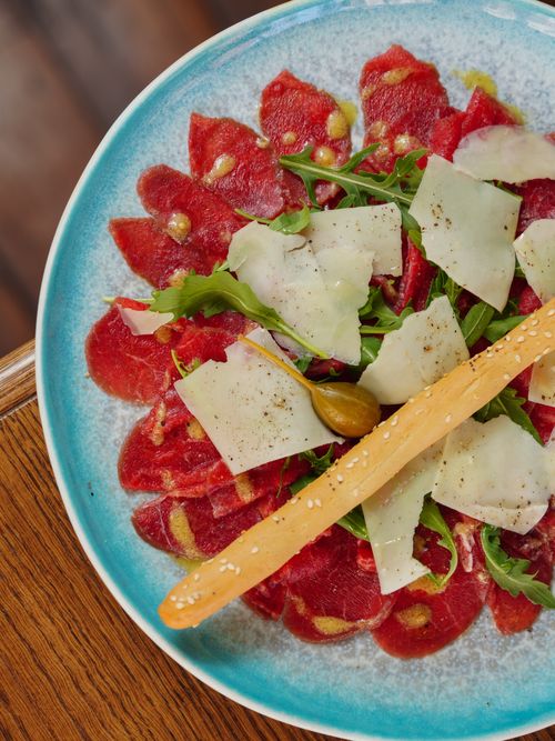 Free Delicious beef carpaccio served with cheese, arugula, and sesame breadstick on a vibrant plate. Stock Photo