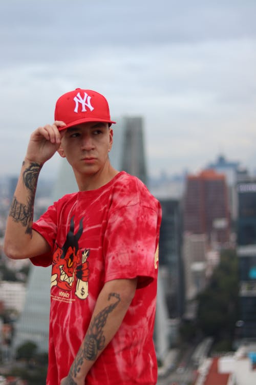 Young Man with Tattoos Wearing a T-shirt and Cap and Posing in City 