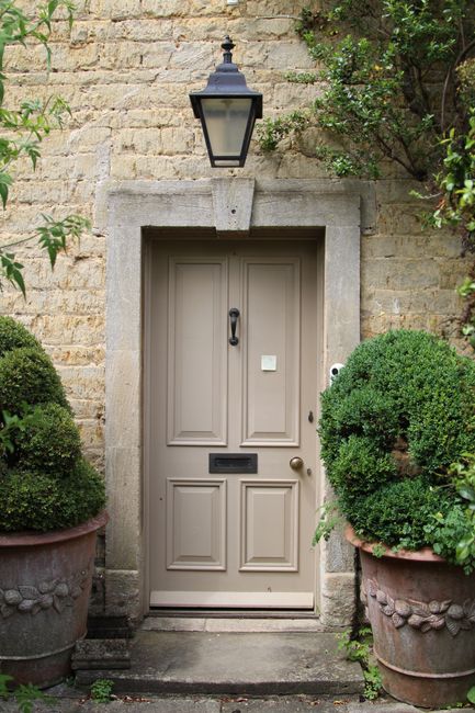 A quaint stone house entrance with a classic wooden door and decorative potted plants flanking the sides.