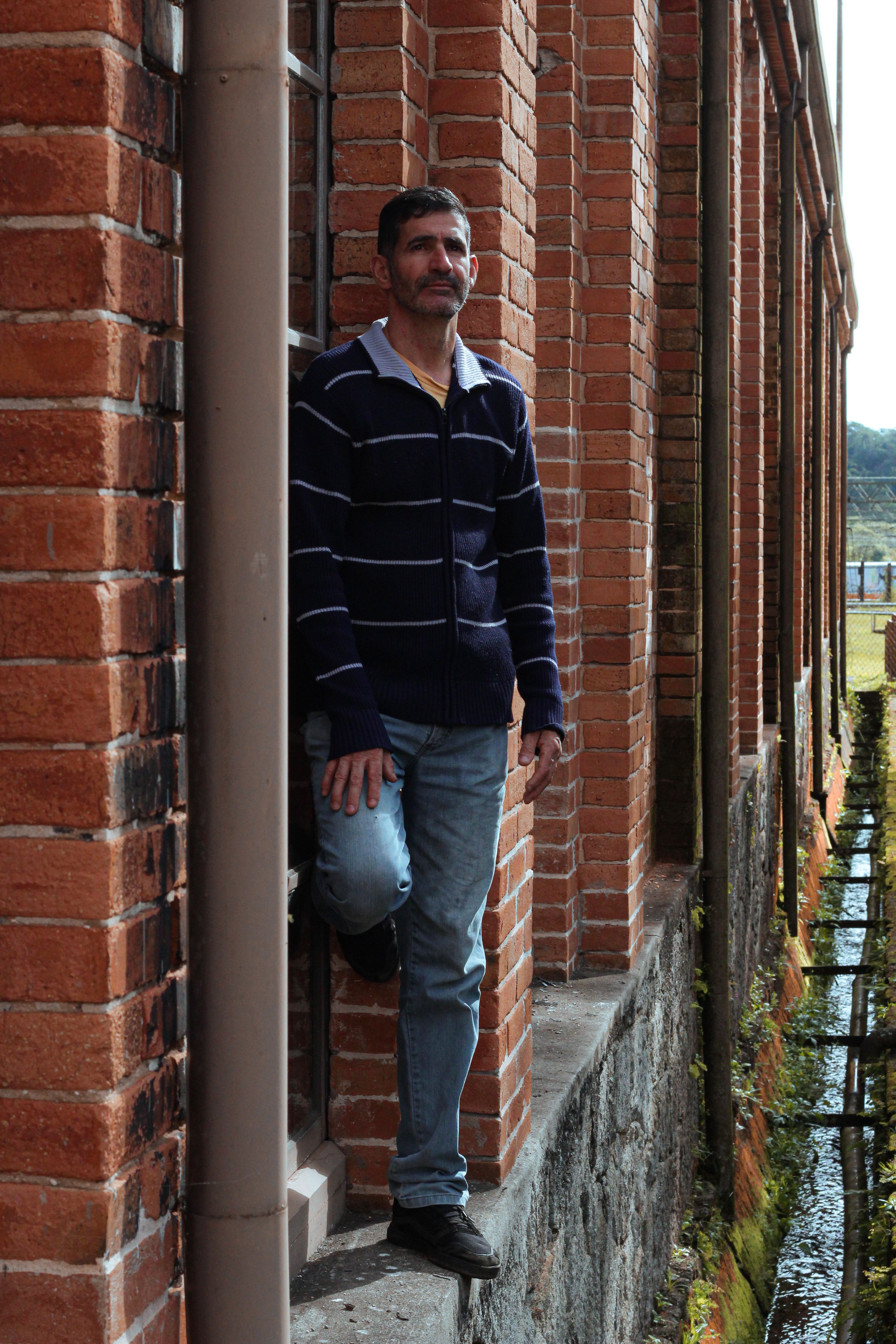 Casual portrait of a man standing by a brick building in an urban setting.
