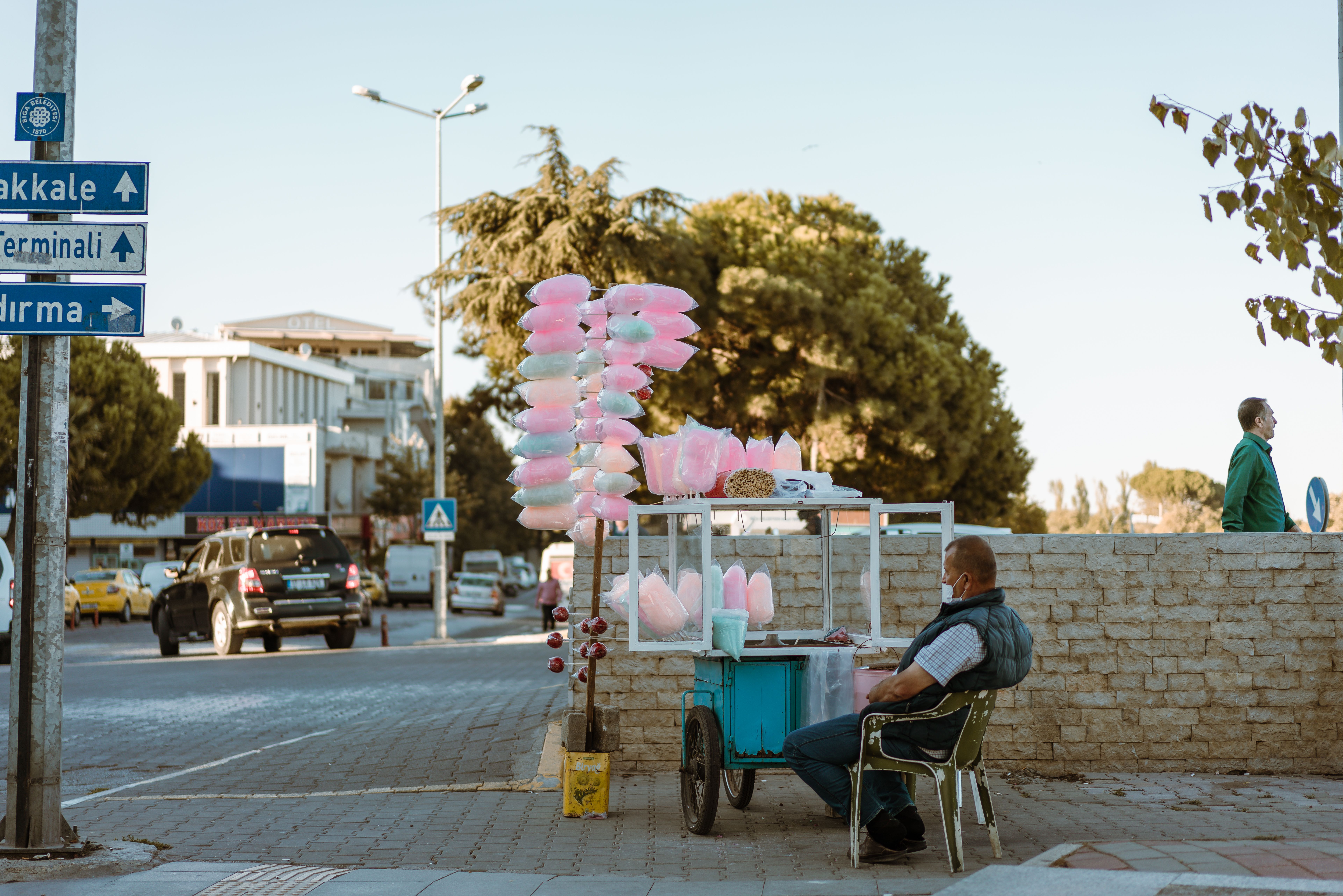 cotton candy machine rental cairo — A street vendor sits beside his cotton candy stand on a busy urban sidewalk.