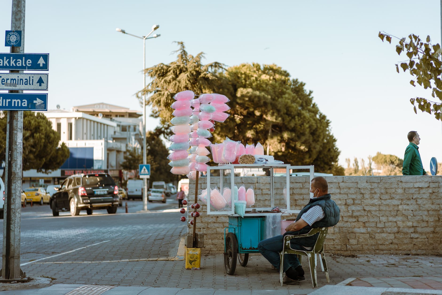cotton candy machine rental cairo — A street vendor sits beside his cotton candy stand on a busy urban sidewalk.