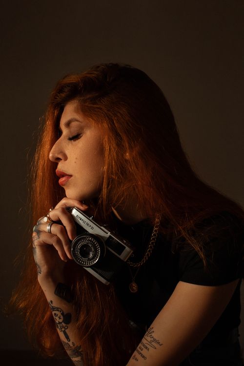 Free Artistic portrait of a redhead woman holding a vintage camera with eyes closed. Stock Photo