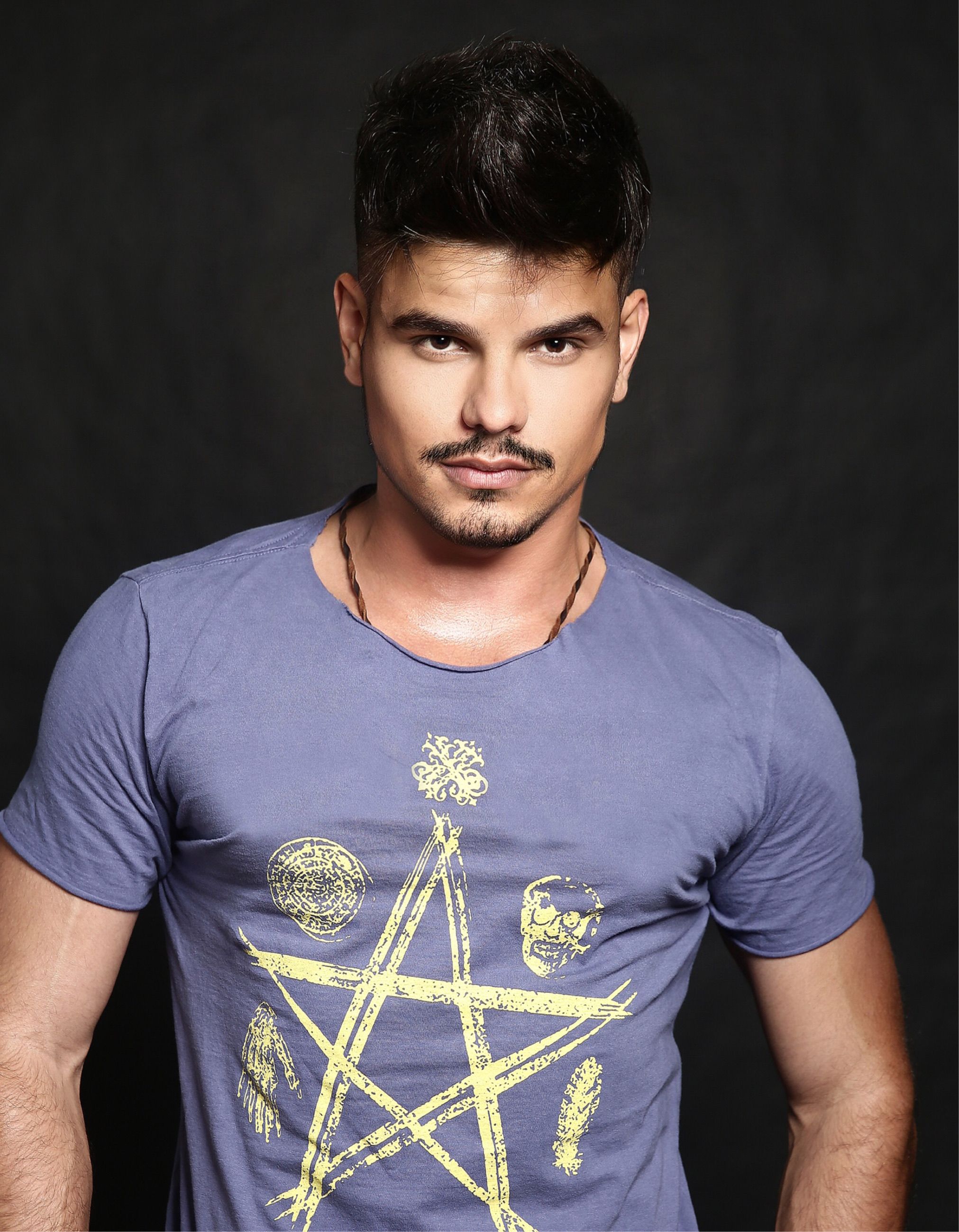 Captivating portrait of a man with a pentagram t-shirt against a black backdrop. Stylish and modern.
