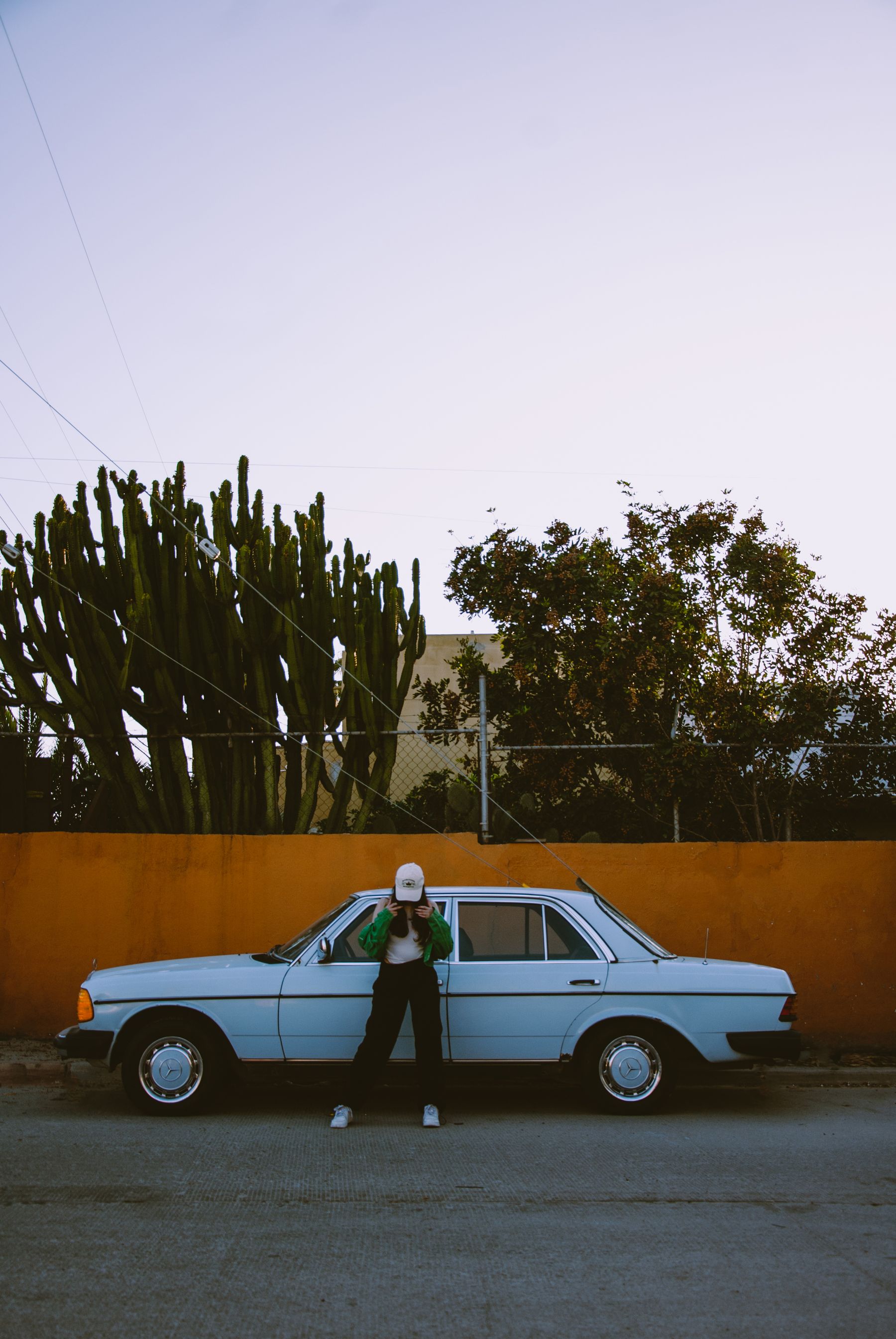 Woman wearing a baseball cap and relaxed streetwear beside a classic car at twilight