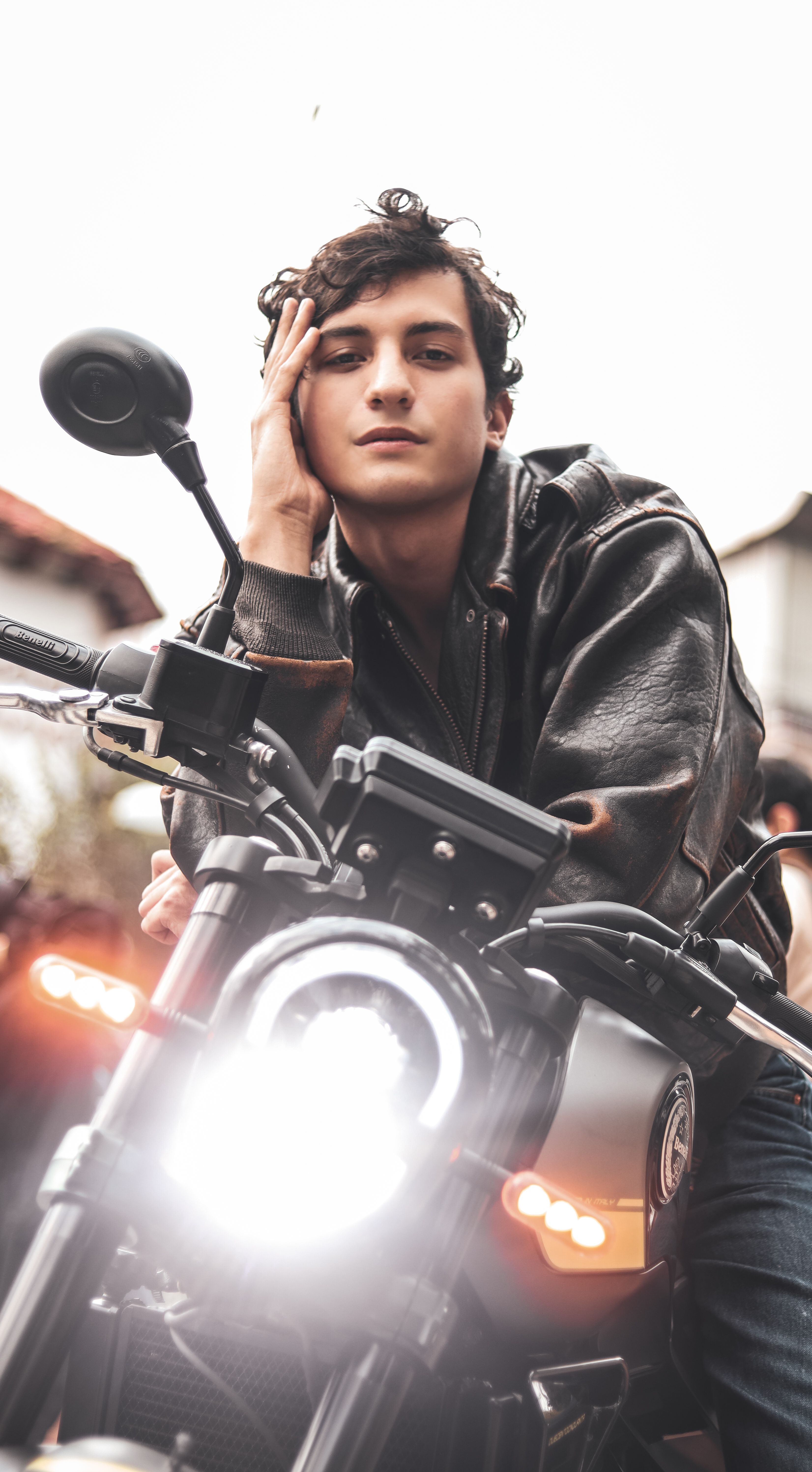 Confident young man in a leather jacket posing with a motorcycle, exuding a cool and adventurous vibe.