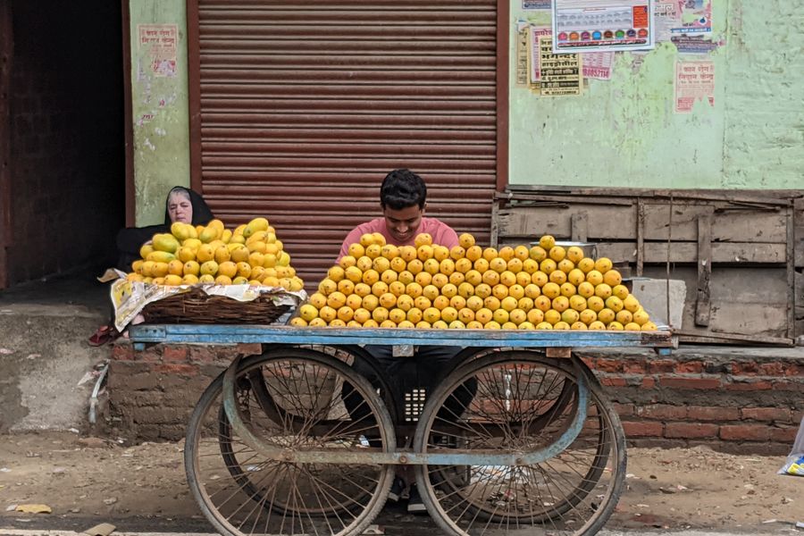 A vibrant street scene in Tanda, India, featuring a vendor selling ripe mangoes from a cart.