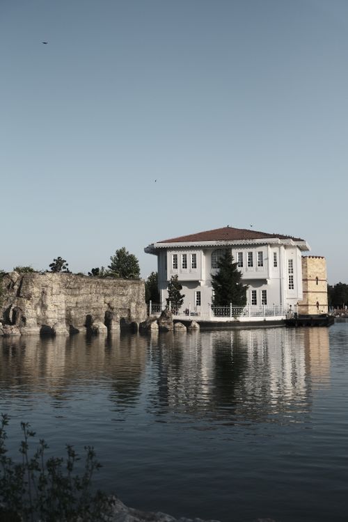 Free A picturesque mansion by a serene lake with clear reflections under a bright sky. Stock Photo