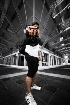 Low angle shot of a young man holding a camera in a modern urban environment.