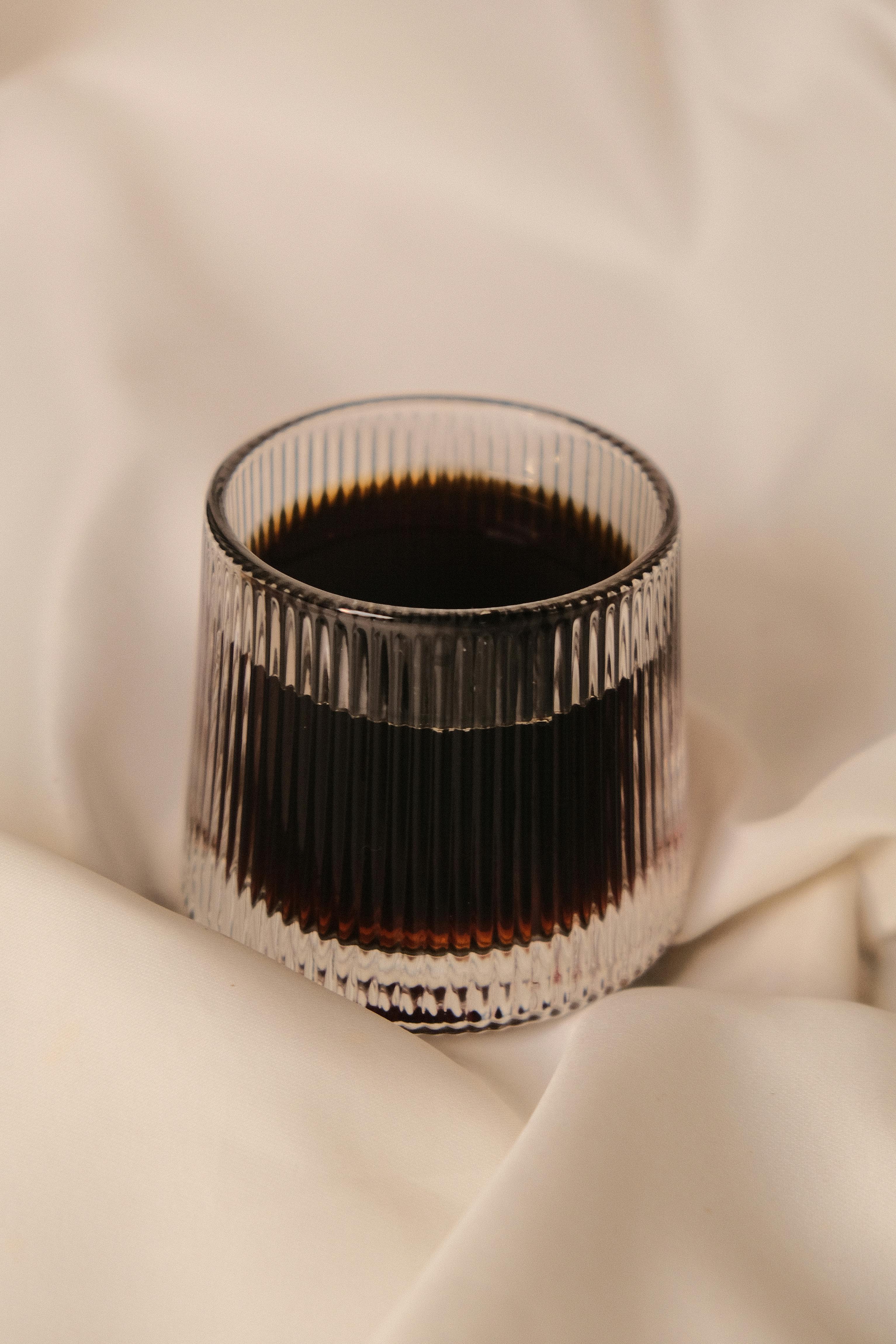 A glass of dark coffee set against a soft fabric background, capturing elegance.