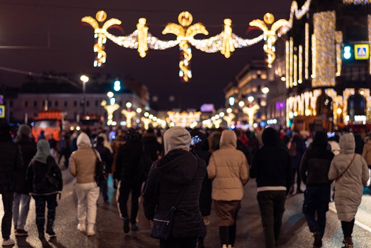 People In Jackets Walking On Decorated Street At Night