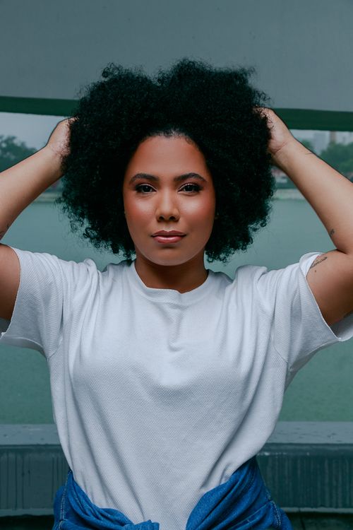 Free A confident woman wearing a white t-shirt poses with hands in her hair, exuding personality and style. Stock Photo