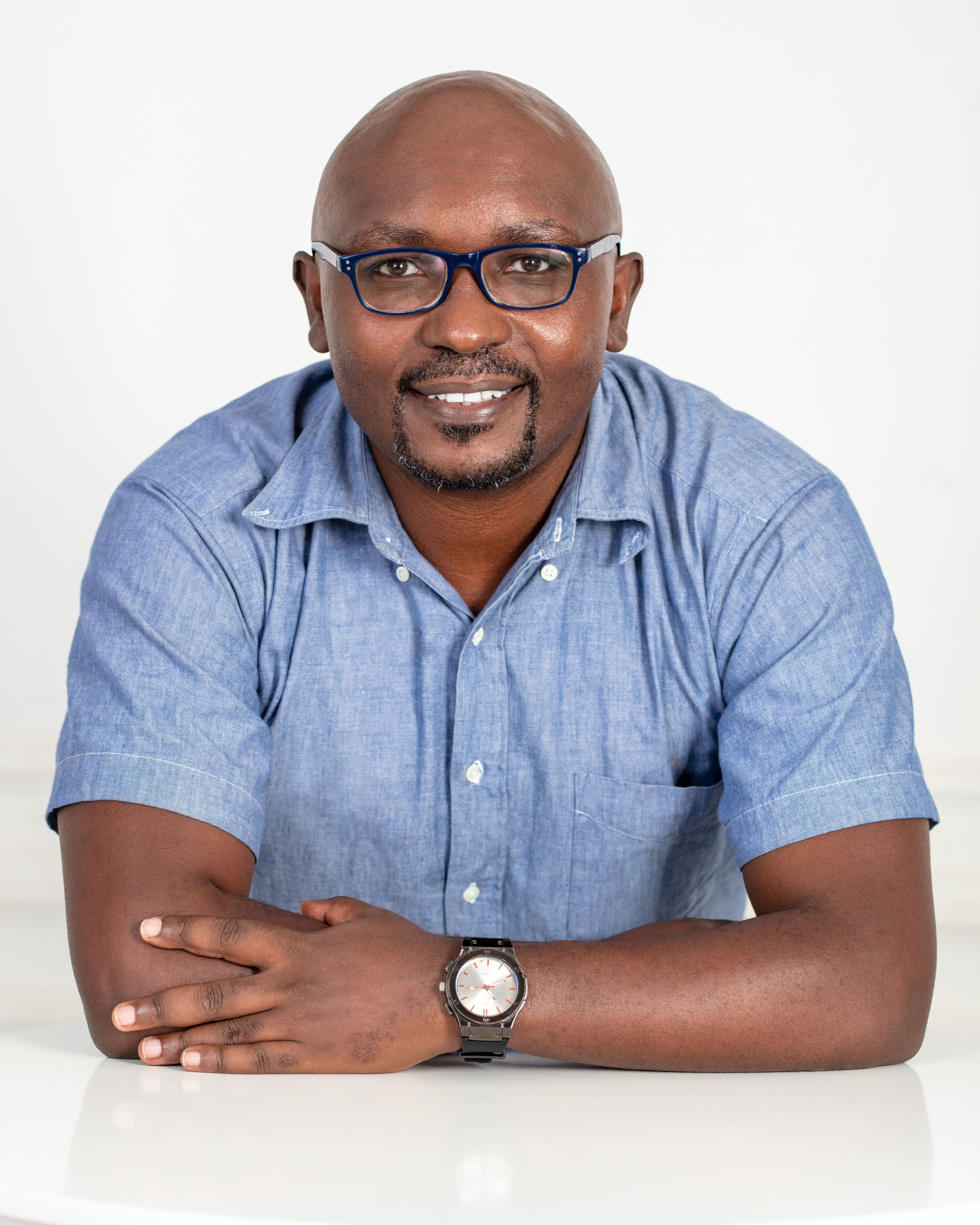 Portrait of a smiling man wearing eyeglasses and a wristwatch in a studio.