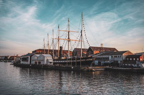 Free A majestic ship in a bustling urban harbor at sunset, reflecting the beauty and history of maritime heritage. Stock Photo