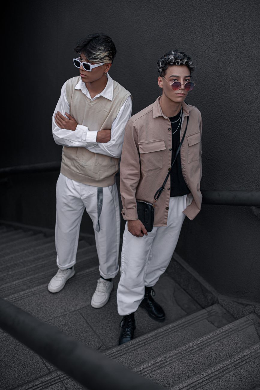 Stylish young men in beige and white outfits posing on stairs, embodying modern fashion trends.