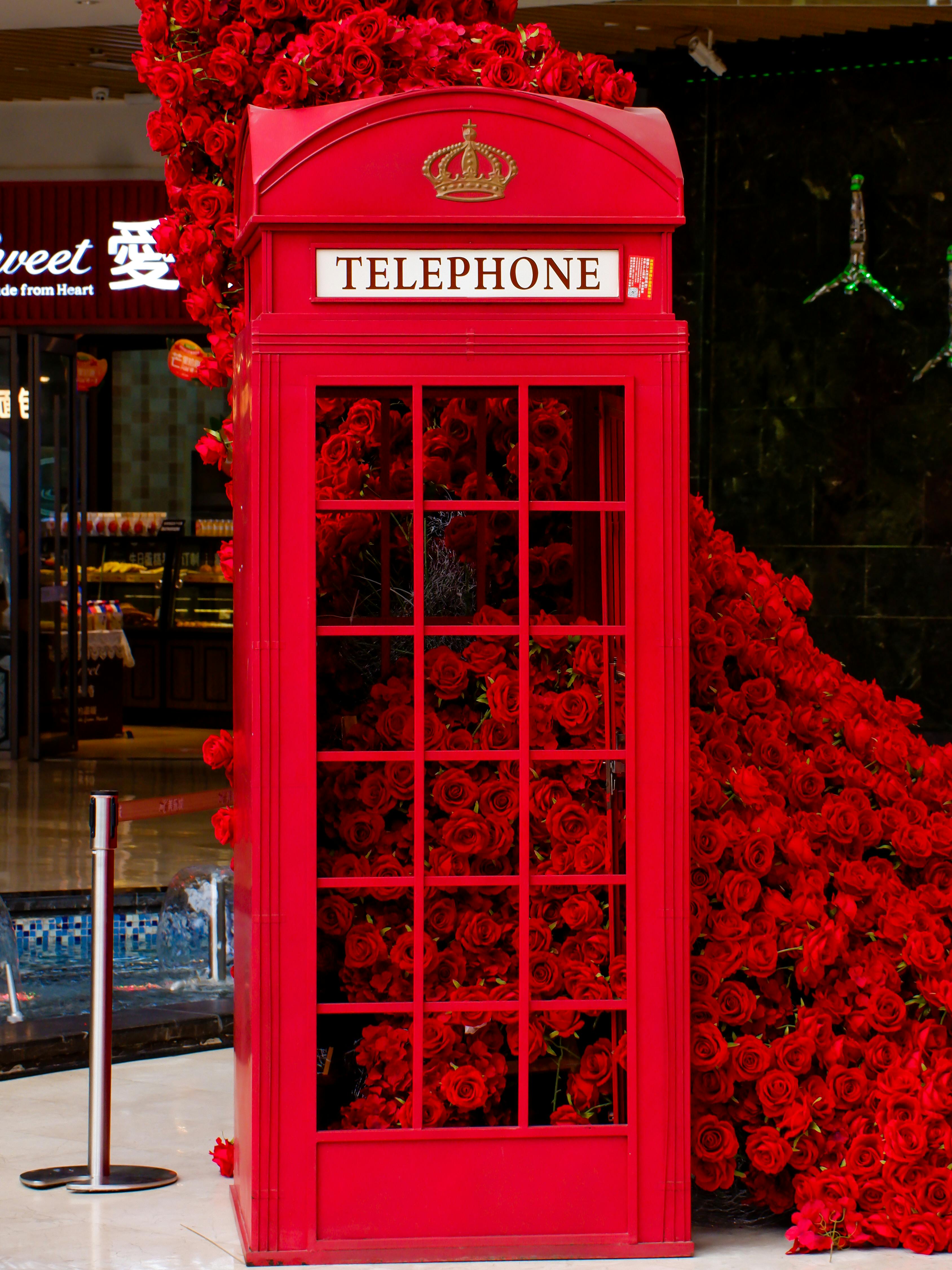 Eye-catching red phone booth overflowing with vibrant roses in a stylish indoor urban environment.