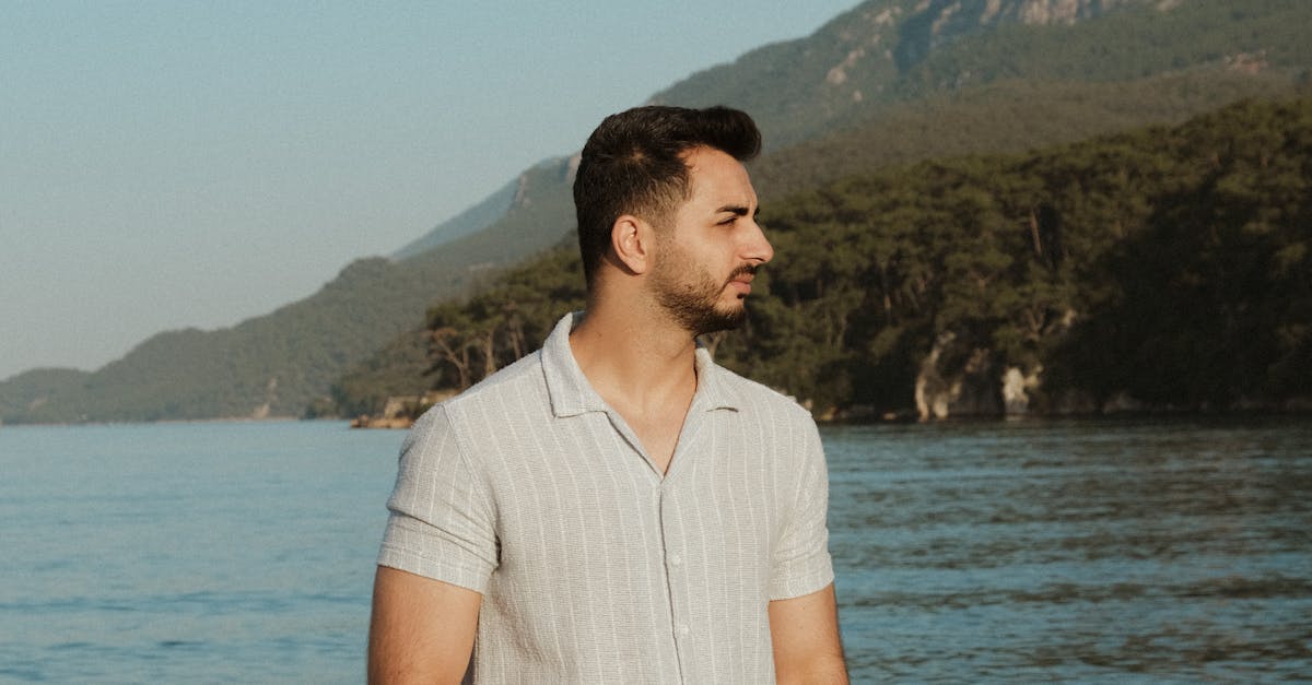 Man in White Short Sleeved Shirt Posing at a Seashore with a Mountain ...