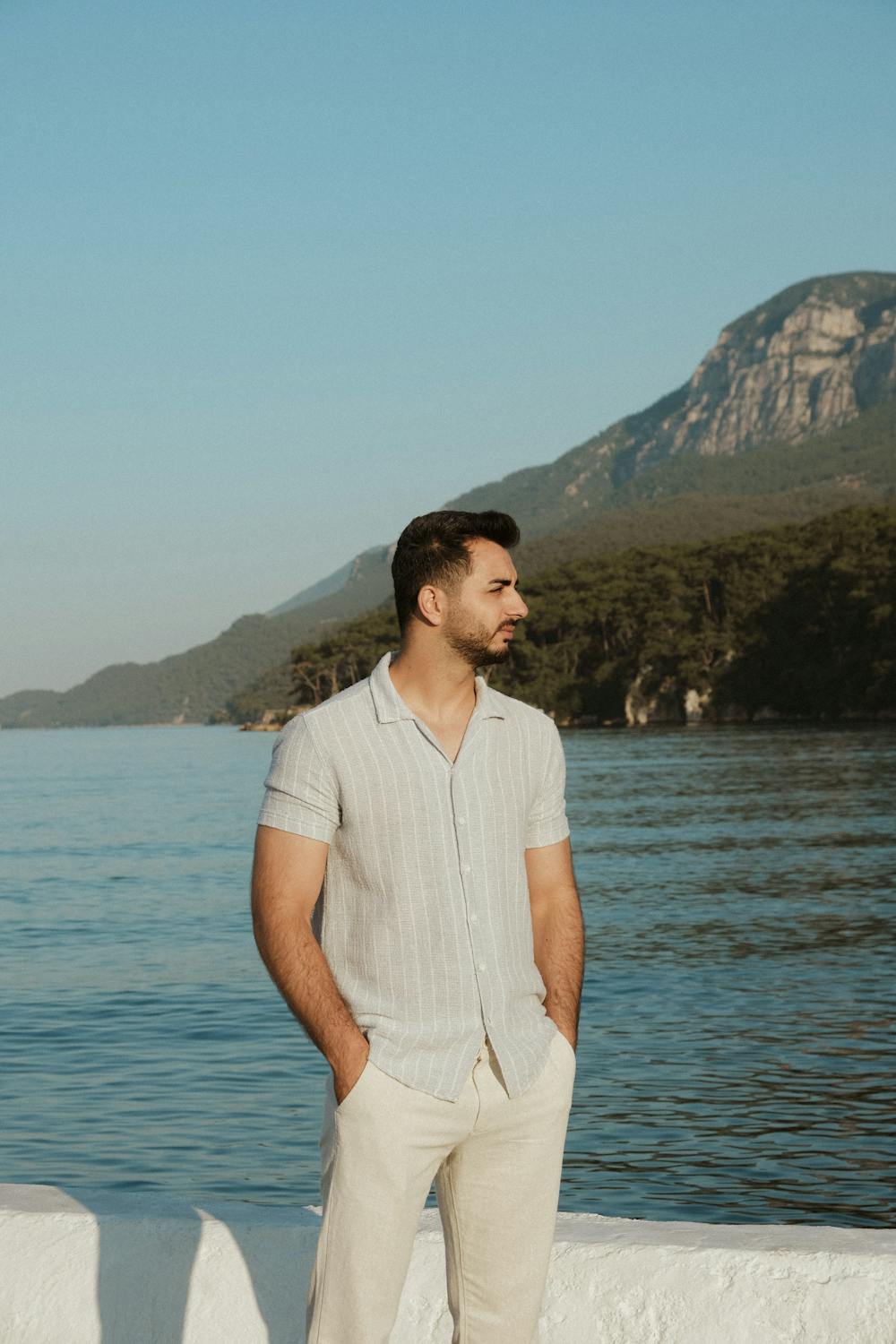 Man in White Short Sleeved Shirt Posing at a Seashore with a Mountain ...