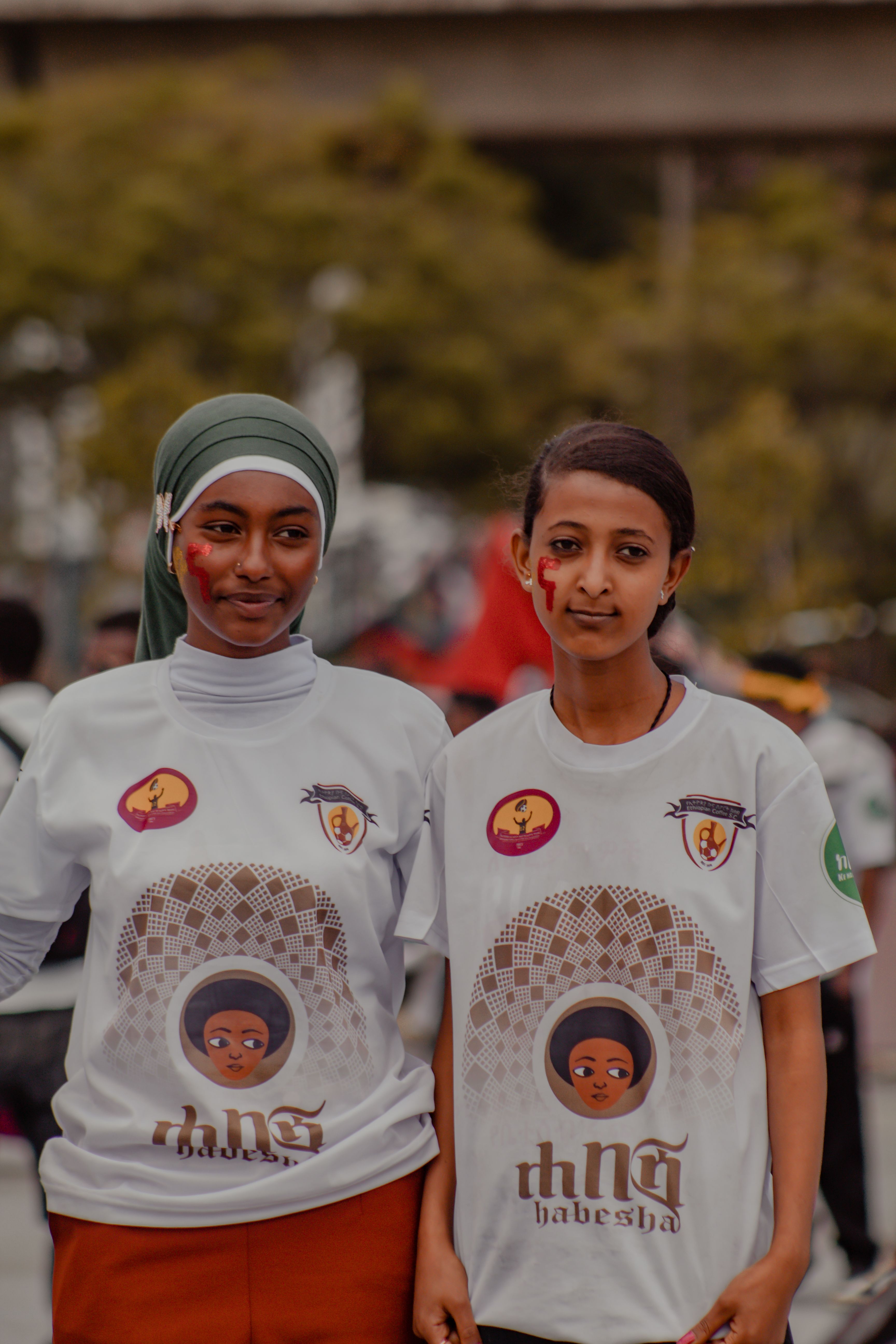 Two Ethiopian women in soccer fan attire with face paint, showing team spirit.