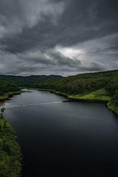 A serene aerial view of a lush forest-bordered lake under dramatic overcast clouds.