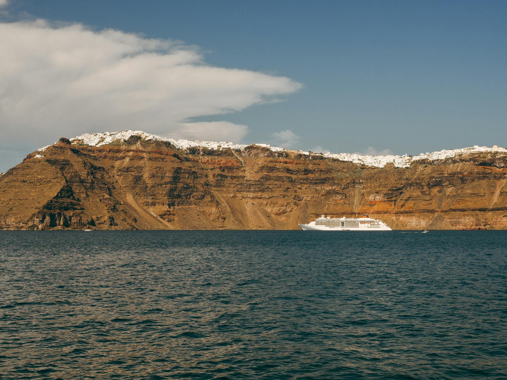 A cruise ship sails by the rugged cliffs of Santorini under a clear sky