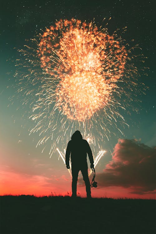 Silhouette Photo of Standing Man Holding Camera Looking at Fireworks Display