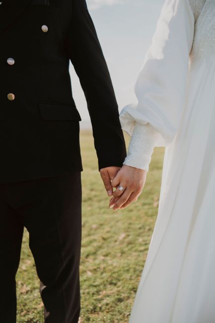 Close-up of a bride and groom holding hands on a sunny day, symbolizing unity and love.
