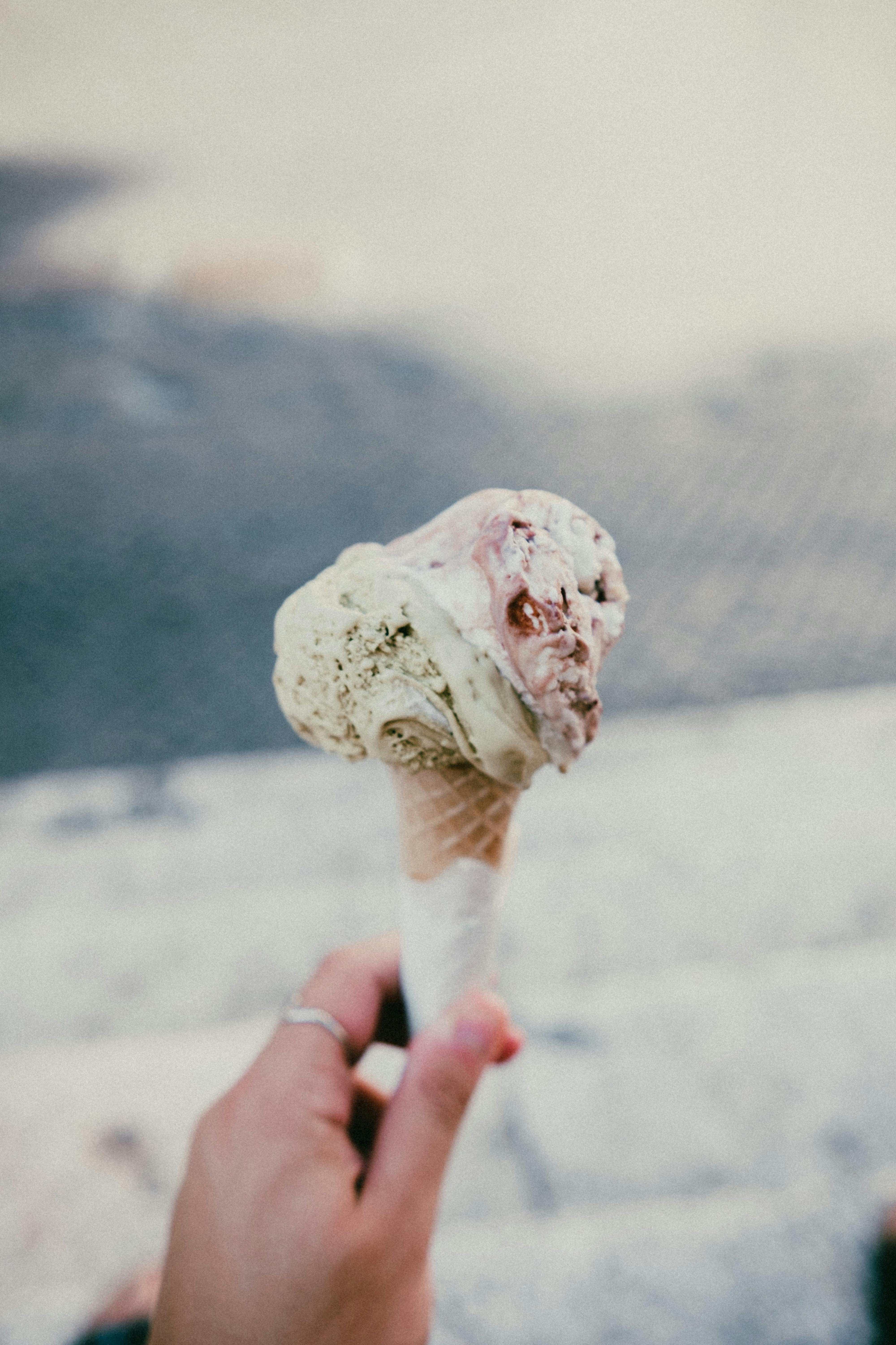 A melting ice cream cone with pistachio and strawberry flavors held outdoors on a summer day.