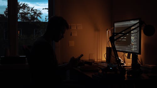 Man Sits by Computer in Dark Room
