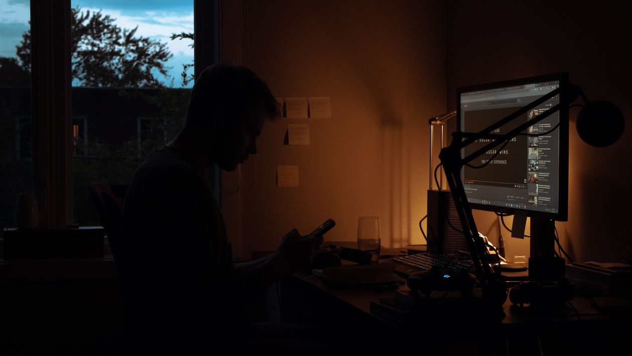 Man Sits by Computer in Dark Room · Free Stock Photo